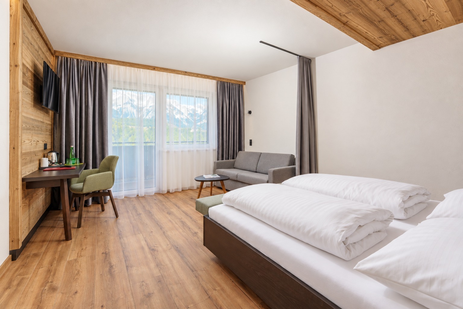 Helles Hotelzimmer mit Holzdecke, Polsterkopfteil und raumhohen Vorhängen