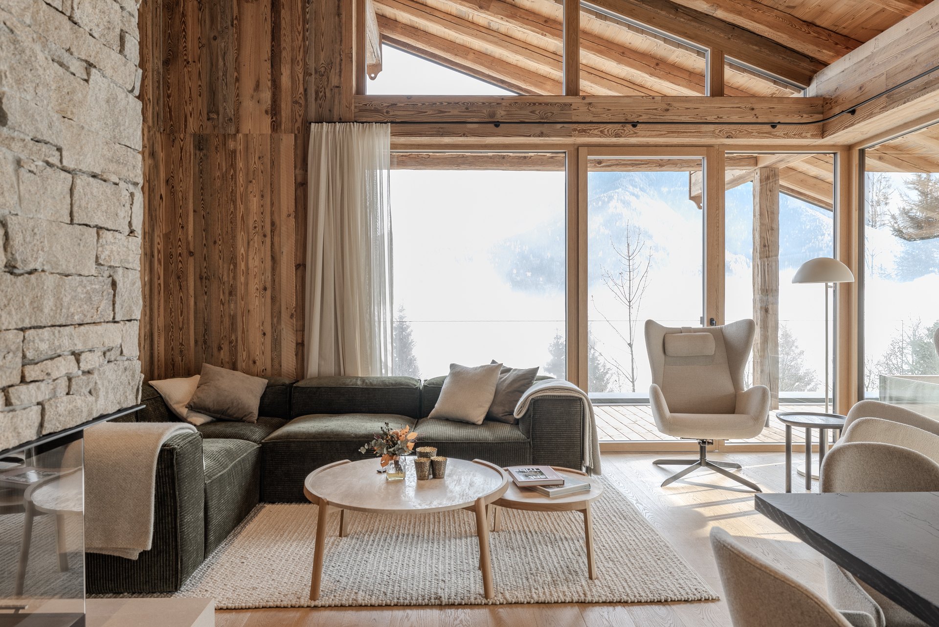 Wohnbereich mit Natursteinwand, grauem Sofa und raumhohen Vorhängen